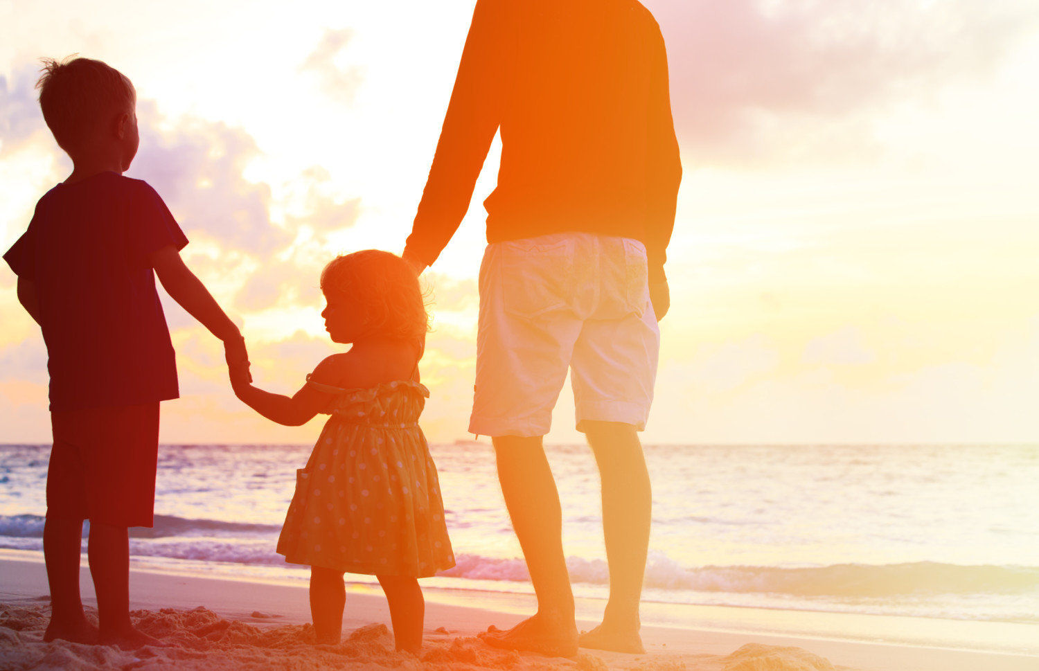 father and two kids walking on beach at sunset